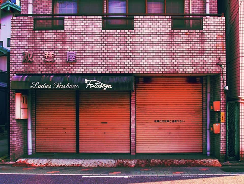 Closed pink shutters line a tiled clothing shop beneath a dark awning with cursive white lettering.