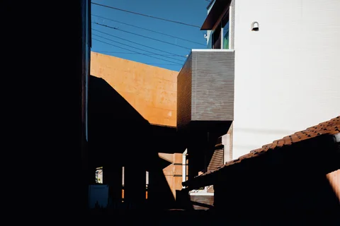 White and orange building walls frame a deeply shadowed passage beneath blue sky.
