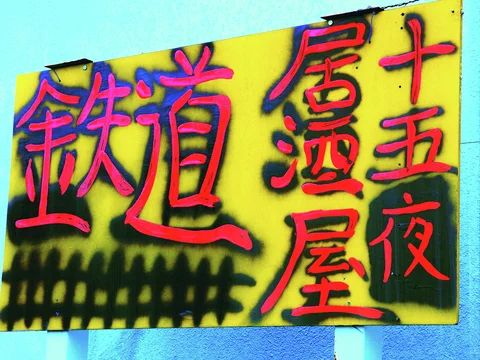 Bold red Japanese lettering with dark outlines fills a yellow sign mounted against turquoise walls.