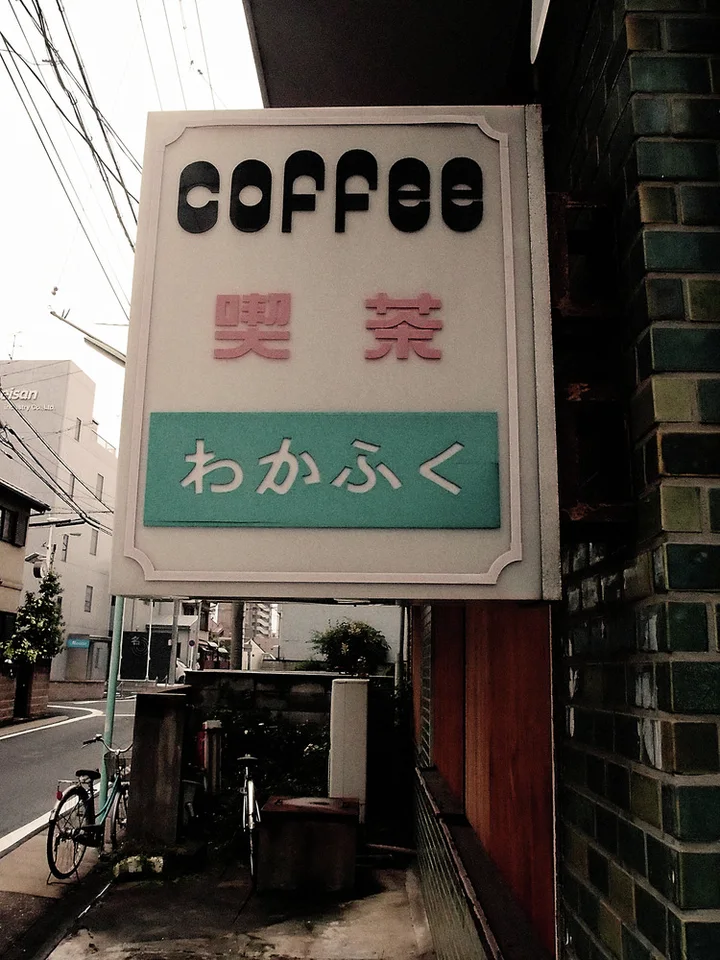 A pale coffee sign with dark lettering and a green lower panel projects above a narrow sidewalk.