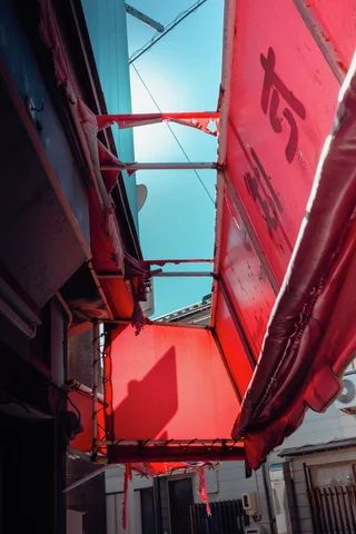 Red translucent awning panels and metal supports frame a narrow strip of bright turquoise sky.