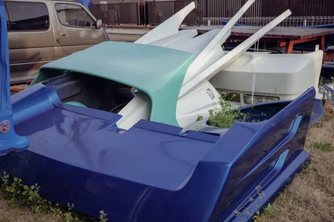 Blue and turquoise molded vehicle panels with long white fins lie piled beside a parked van.