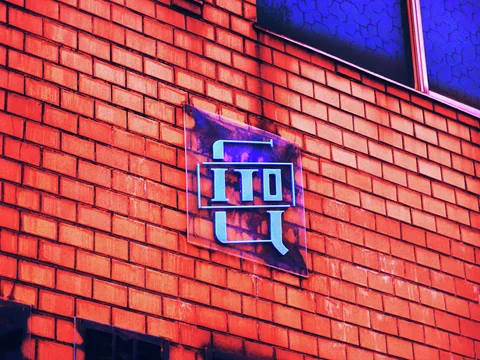 A small dark plaque bearing a pale blue character hangs on a vivid red brick wall.