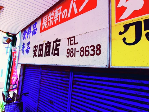 A long pale shop sign with Japanese lettering and a phone number hangs above vivid blue shutters.