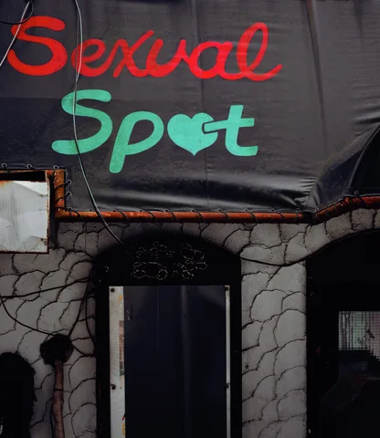 Red and green lettering on a black awning hangs above a dark doorway framed by stone-patterned walls.