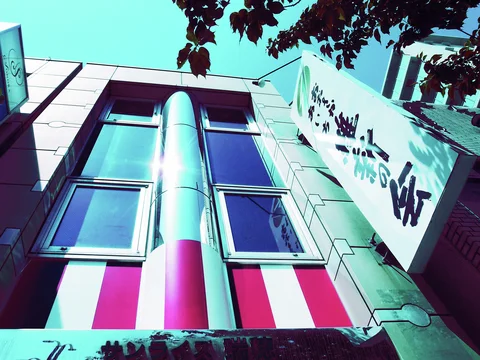A tall silver column separates paired windows on a pink facade beside a projecting white sign.