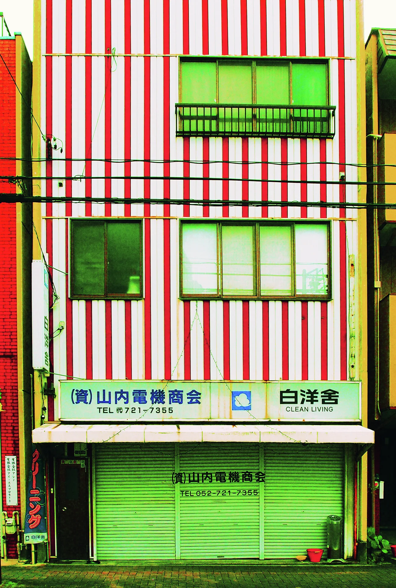 Red and white vertical stripes cover a narrow building above closed green storefront shutters.