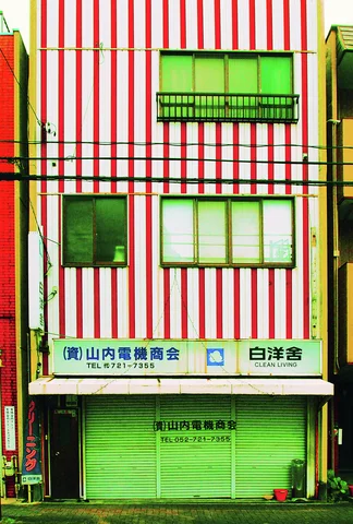 Red and white vertical stripes cover a narrow building above closed green storefront shutters.