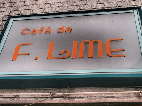Raised orange cafe lettering sits within a turquoise-edged gray sign mounted on textured brickwork.