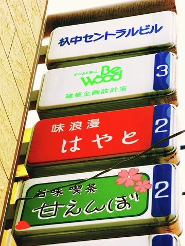 Stacked rectangular business signs project from a wall, with red, green and white panels.
