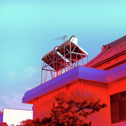 A cylindrical tank rests on a metal rooftop frame above a red-toned building and pruned tree.
