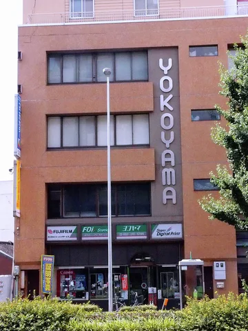 Vertical YOKOYAMA lettering spans a brown building facade above dark windows and street-level shop signs.