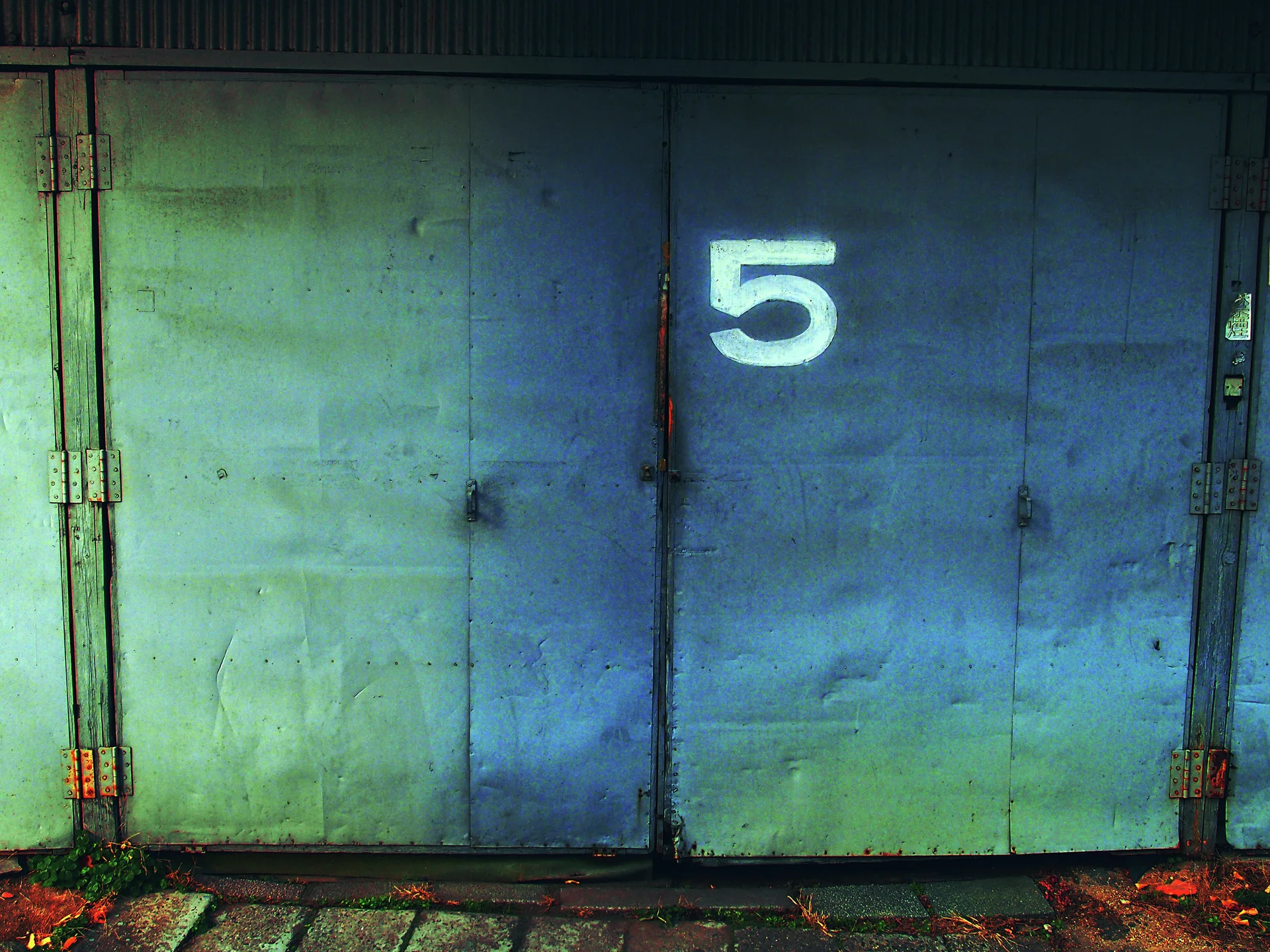 A large white 5 marks weathered blue-green metal double doors with rusted hinges and dark lower edges.