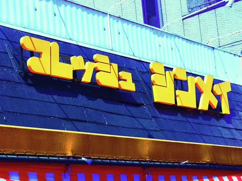 Large yellow Japanese characters project from a dark blue storefront fascia below pale corrugated siding.