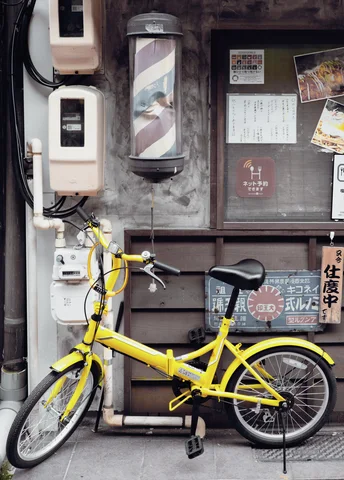 A bright yellow bicycle stands beneath a weathered barber pole beside utility boxes and posted notices.