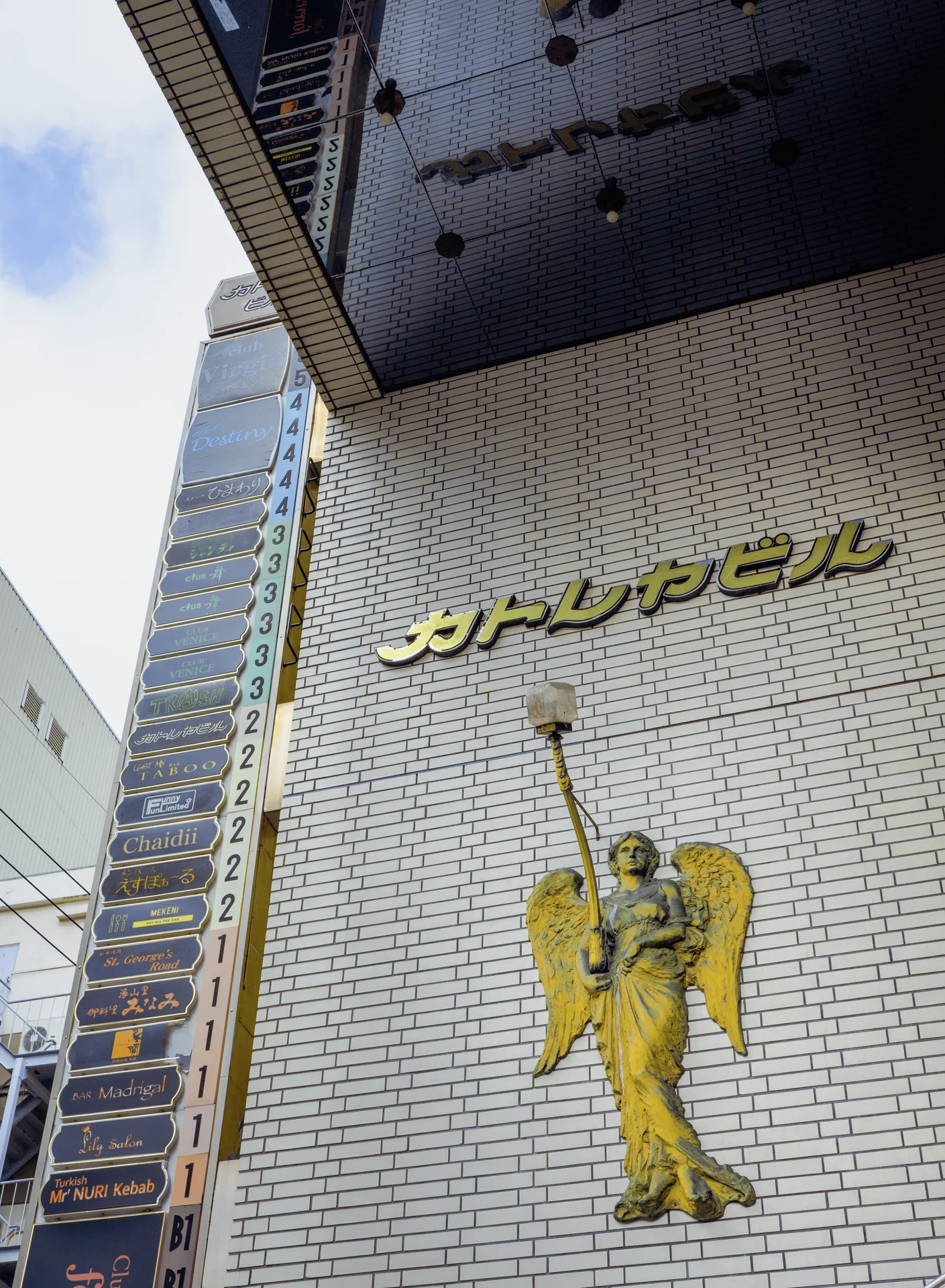 A gold winged figure decorates a tall white brick-patterned facade beneath raised Japanese lettering.
