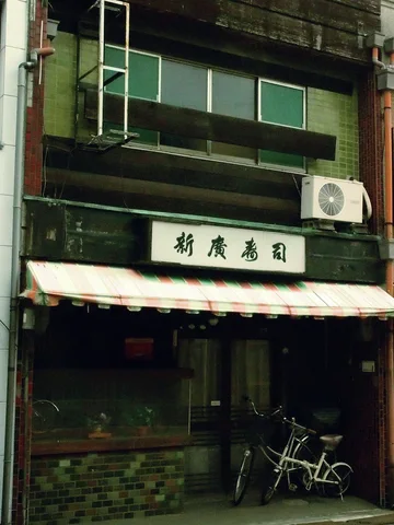 A bicycle stands beneath a striped awning on a dark wooden shop facade.