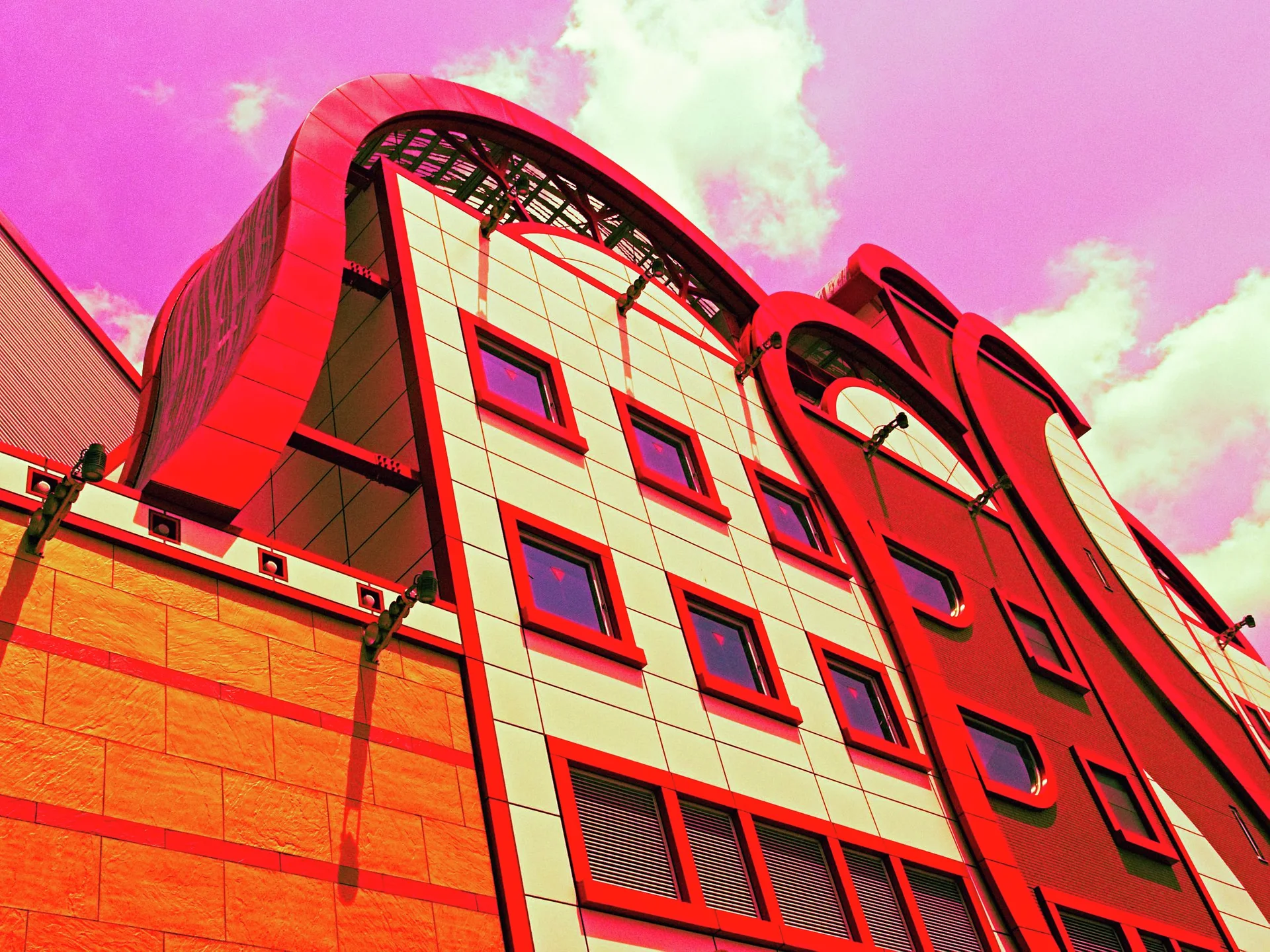 Sweeping red arches frame rectangular windows on a tall building beneath a pink-toned sky.