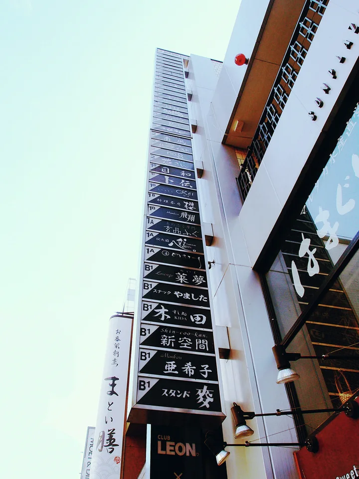 A tall narrow directory of stacked black business signs projects from a white building facade.
