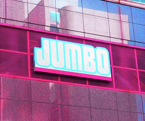 Large white JUMBO letters outlined in turquoise sit on a bright pink panel beneath reflective windows.