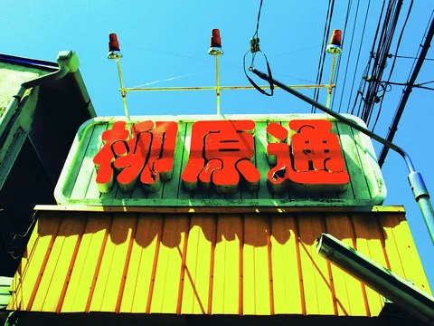 Large red characters stand above a yellow corrugated facade beneath small lamps and tangled overhead wires.