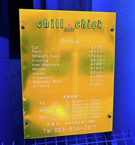 A reflective gold salon price plaque is mounted against a vivid blue wall.