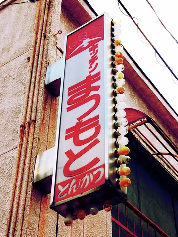 A red and white vertical sign bordered by bulbs hangs beside a weathered wall.
