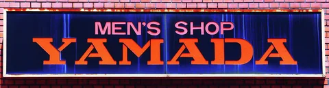 Orange YAMADA lettering and smaller pink MEN'S SHOP text fill a long dark blue sign.