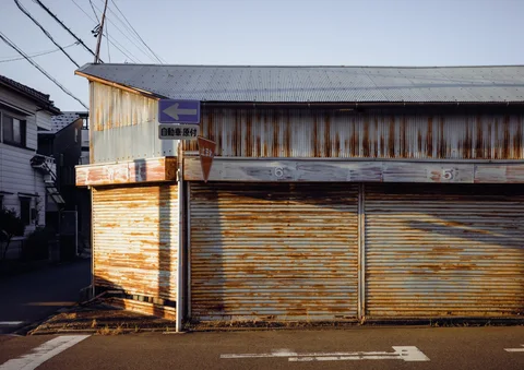 Rust streaks cover the closed shutters and corrugated facade of a low street-corner building.