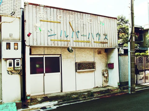 Faded lettering covers a weathered pale shop facade above double doors, a small window and exposed utility meters.