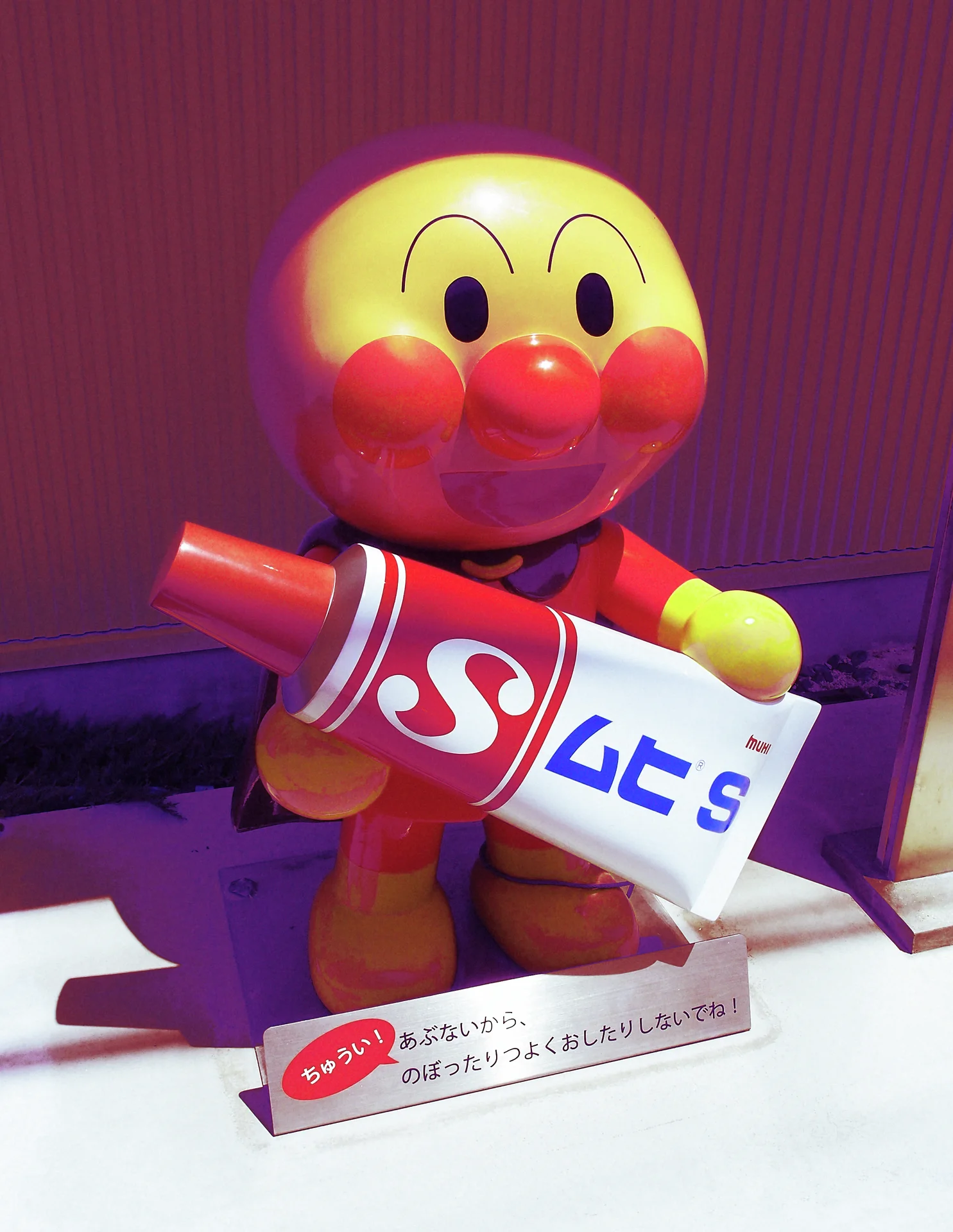 A smiling round-headed cartoon figure holds an oversized red and white bottle on a display counter.