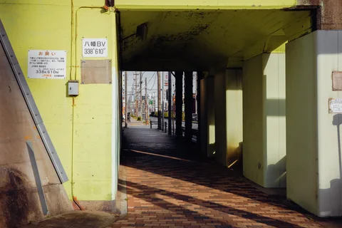 Sunlight casts long diagonal shadows through a covered passage with pale yellow pillars and walls.