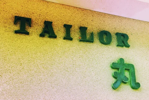 Raised green Tailor lettering and a Japanese character mark a textured yellow and pale wall.
