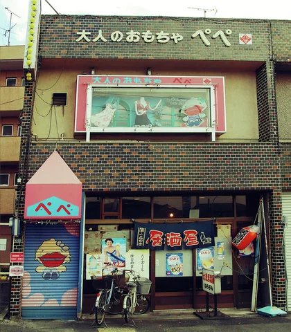 Colorful signs and window graphics fill a dark tiled shop facade with a bicycle parked beside its entrance.