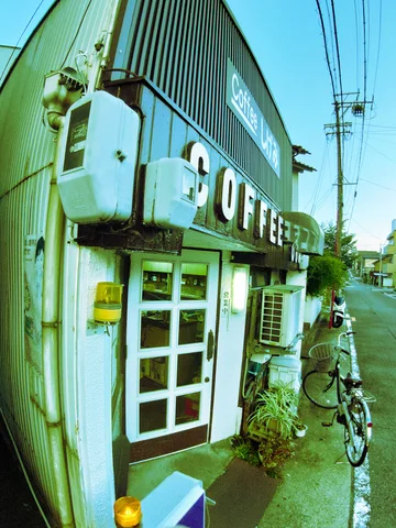 Large raised COFFEE letters span a small weathered storefront beside a bicycle and wall-mounted air conditioners.