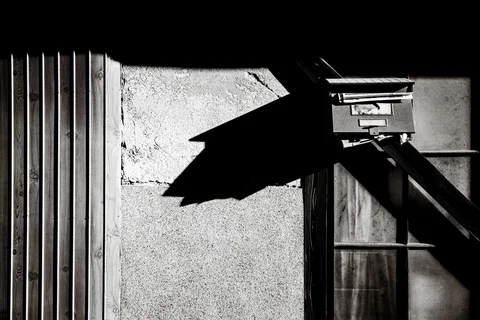A projecting mailbox casts a crisp angular shadow across a textured wall in black and white.