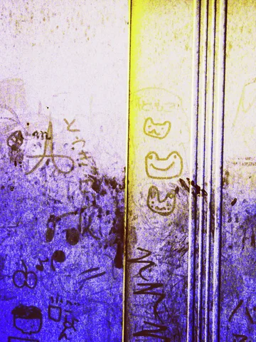 Small graffiti faces and scribbled marks cover a stained wall beside narrow vertical metal strips.
