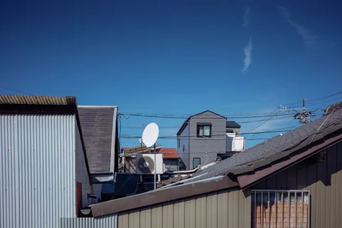 Closely spaced rooftops surround a white satellite dish beneath a deep blue sky with wispy clouds.