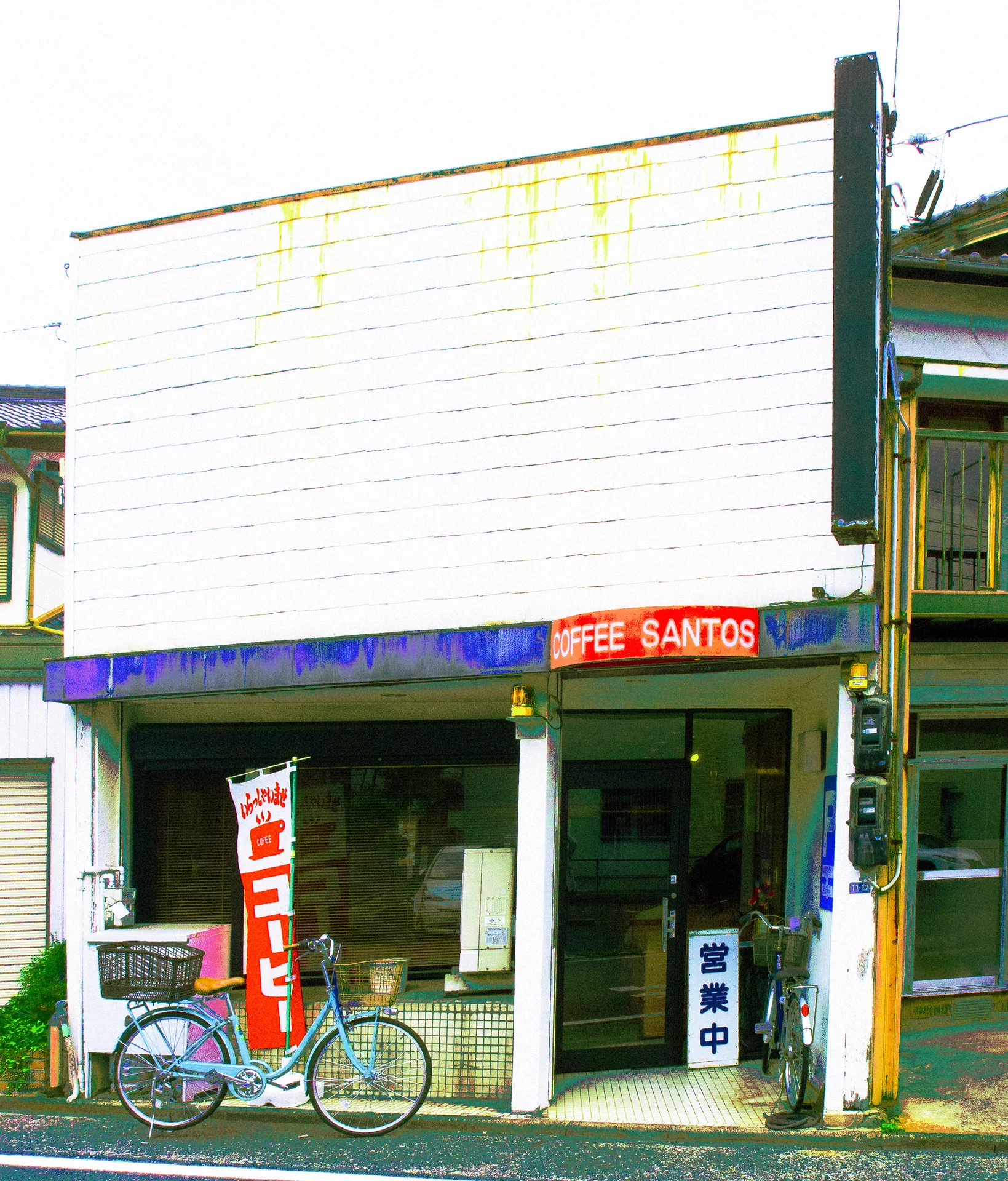 A bicycle stands outside a small coffee shop beneath a broad pale facade and blue awning.