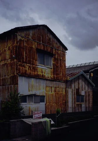 Rust streaks cover corrugated buildings with small windows beneath a cloudy gray sky.