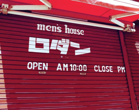 White men's house lettering and Japanese characters decorate a red shutter beneath a red awning.