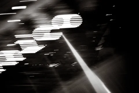 Bright white light trails form overlapping segmented shapes across a dark blurred black and white scene.