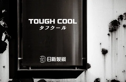 A dark TOUGH COOL sign projects from a stained pale wall in black and white.