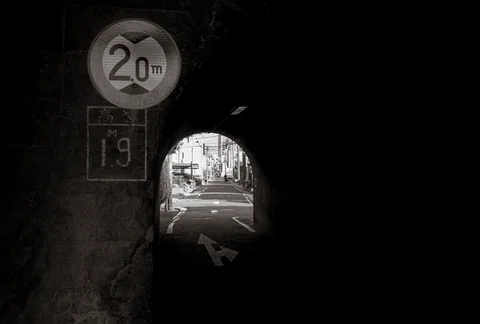 A low arched passage frames a bright street beneath a circular height-limit sign and painted road arrow.