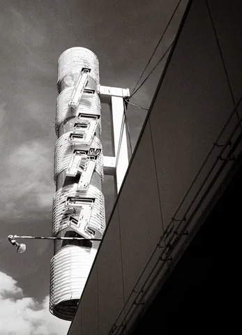 Raised characters run down a cylindrical projecting sign beside a dark building facade in black and white.