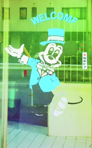 A turquoise cartoon character in a top hat decorates a glass door beneath curved welcome lettering.