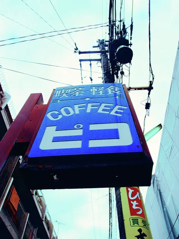 A blue projecting COFFEE sign with white Japanese characters hangs beneath a cable-covered utility pole.