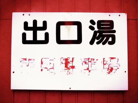 Bold black Japanese characters fill a pale rectangular sign above faded red lettering on a red wall.