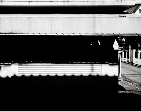 A closed shutter sits beneath a deep dark awning on a corner building in black and white.