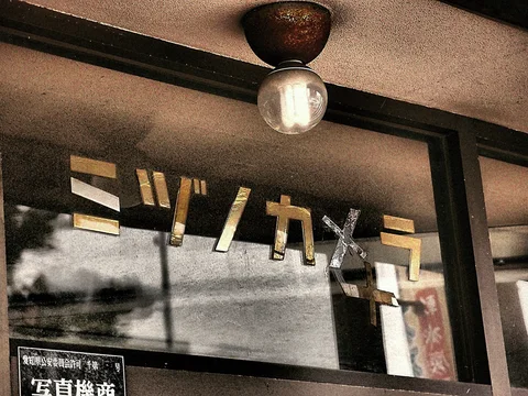 Gold Japanese lettering crosses reflective shop glass beneath a round bulb and dark metal frame.